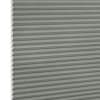 Cellular honeycomb blind, light gray with visible hexagonal cell ends at the left edge; closed and fully lowered into tight horizontal pleats; interior setting with soft diffuse lighting, no visible view.