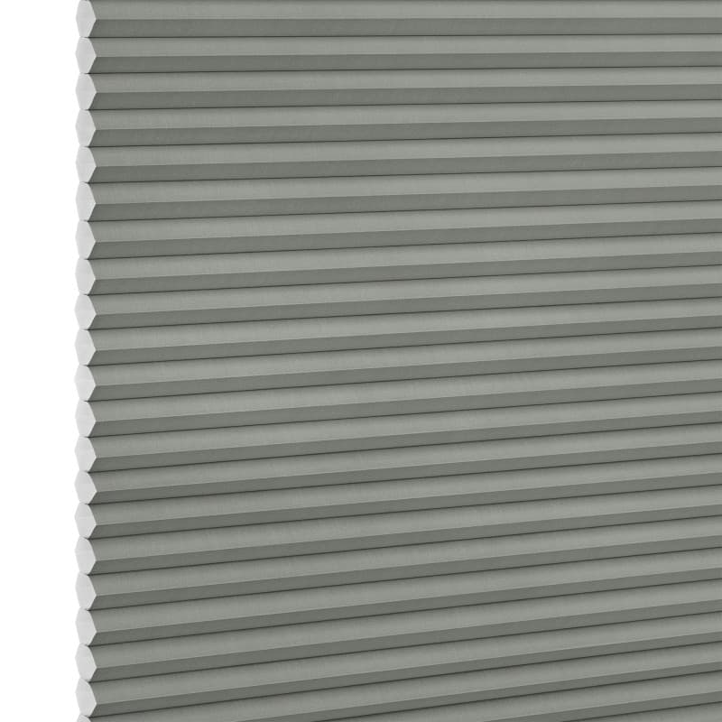Cellular honeycomb blind, light gray with visible hexagonal cell ends at the left edge; closed and fully lowered into tight horizontal pleats; interior setting with soft diffuse lighting, no visible view.
