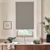 Roller blind covers most of a kitchen window above a stainless sink, with countertop, faucet, leafy plants, framed sketch on wall and wooden cabinets below.