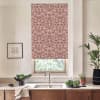 Patterned red floral roller blind hangs lowered over a kitchen window, filtering light; stainless faucet and sink sit below on a countertop with bowls of cabbage and a potted plant nearby.