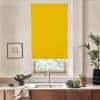 Yellow roller blind covers most of kitchen window above stainless sink; light filters below, countertop holds bowl of leafy greens, potted plants, a towel, and a framed sketch on the wall.