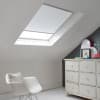 Room with white eaves wall, dark blue-grey wall to right with a shabby chic white drawer unit, a contemporary white chair, white painted floorboards and a skylight blind in snow white.