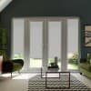White-framed patio doors with light-gray roller blinds partially lowered, standing between green velvet armchairs; glass coffee table on black-and-white chevron rug, garden glimpsed below blinds.