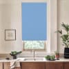 Blue roller blind covers a kitchen window, partially lowered over greenery outside; stainless faucet above sink, wooden cabinets below, bowl of leafy vegetables and potted plants on the countertop.