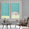 Turquoise, leaf-patterned roller blinds covering two sash windows—one fully lowered, one halfway—filtering soft daylight; living-room setting with gray walls, rattan armchair, patterned cushion, wooden coffee table and ceramics, garden view.