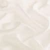 A soft off-white fabric sheet with gentle folds and shallow depressions; rumpled and draped, creating subtle shadows — close-up under diffuse, warm lighting against a neutral background.