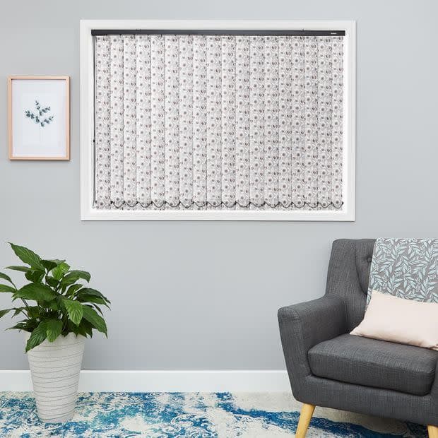 Sheer white lace curtain, fitted inside the window frame with floral pattern and scalloped hem—hanging closed, softly filtering daylight in a light-gray living room with gray armchair, potted plant, and blue rug.