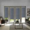 Gray roller blinds cover French doors and sidelights, textured panels with two bottoms slightly raised to show lawn. They are lowered, filtering daylight. Living room with armchair, sofa, coffee table.