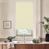 Cream roller blind hangs over a window above a stainless sink; chrome faucet centered. Countertop holds bowls and plates of greens, a towel, framed sketch left, tall potted plant right.