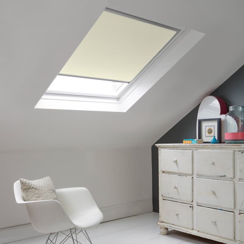 Room with white eaves wall, dark blue-grey wall to right with a shabby chic white drawer unit, a contemporary white chair, white painted floorboards and a skylight blind in ivory.
