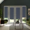 Patio doors with four navy roller blinds lowered halfway, framing a sunlit garden; glass coffee table on chevron rug sits between two green armchairs in a modern pitched-roof living room.