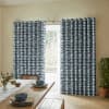 Blue-gray, horizontally striped grommet-top curtains hung on a metal rod, mostly closed with a central gap revealing a glass door; sunlit dining room with wooden table, bench, and potted plant.
