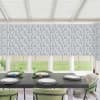 Dining table set with four place settings and decorative green glassware, positioned in a sunlit conservatory with green velvet chairs, patterned Roman blinds, and a grassy backyard visible beyond.