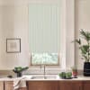 Window blind hangs down, filtering light over a kitchen sink; stainless faucet centered on marble countertop surrounded by bowls of leafy greens, potted plants, framed sketch on wall, wooden cabinets.