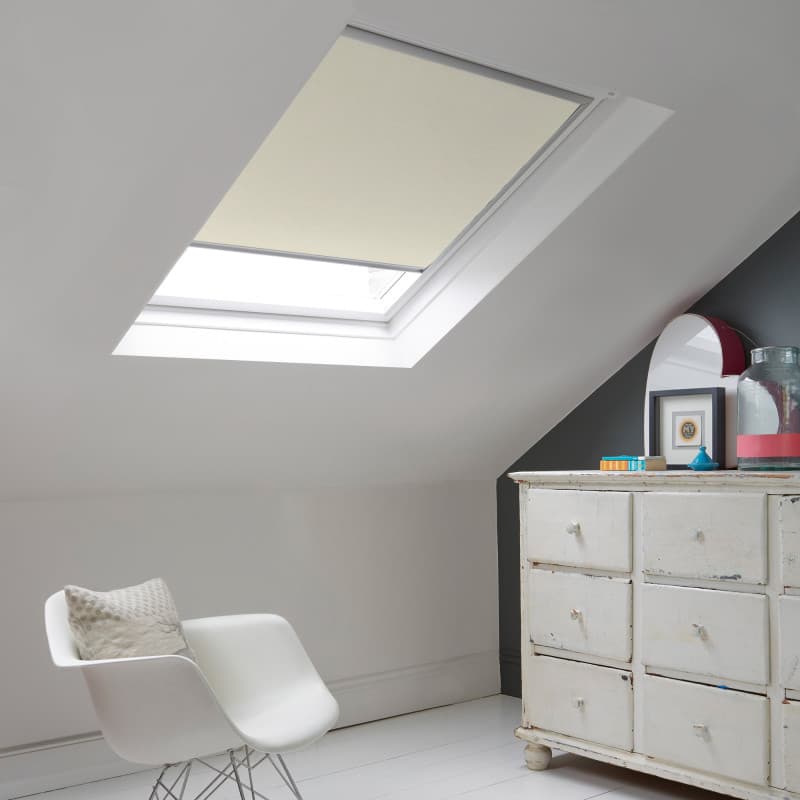 Room with white eaves wall, dark blue-grey wall to right with a shabby chic white drawer unit, a contemporary white chair, white painted floorboards and a skylight blind in linen-cream.