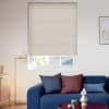 Beige cellular (honeycomb) blind, fully lowered with a narrow bottom gap showing outside roof; filtering soft daylight. Context: minimalist living room with blue sofa, cushions, floor lamp and sideboard.