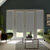 French glass doors with grey roller blinds lowered, letting narrow garden light through; situated in a living room with green armchairs, a glass coffee table and a chevron-patterned rug.