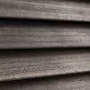 Horizontal wooden blinds, narrow slatted wood shown in close-up; closed and overlapping, textured grain visible; filtering/diffusing light in a dim interior setting with neutral gray‑brown tones.