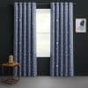 Grommet-top navy curtains patterned with moons and stars, hung on a metal rod, parted to admit soft daylight; dark-painted room with wooden side table, dome lamp, abstract print.