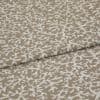 Beige woven fabric with a white, branch-like pattern folded across itself, shown close-up on a flat surface under soft, even lighting.