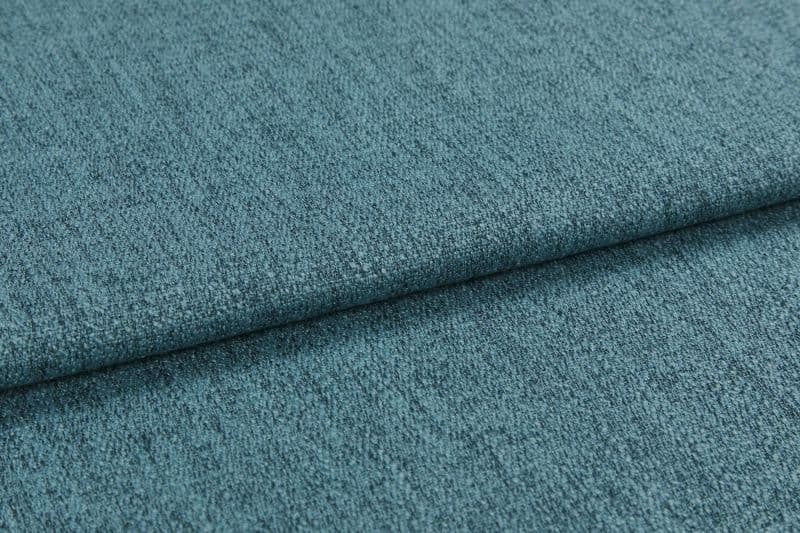 Teal textured upholstery fabric, folded into overlapping layers with visible weave and nap; lying flat as a close-up sample under soft diffuse lighting, showing subtle color variation.