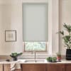 A pale roller blind covers the upper half of a kitchen window, filtering daylight; below, stainless faucet and sink sit on wood countertop with bowls, plants and a towel.