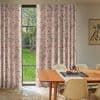 Floor-length pink patterned curtains (crane and blossom motif) hung either side of a tall black-framed window, drawn mostly closed with a central gap, filtering soft daylight into a dining room.