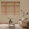 Horizontal tan Venetian blinds, fully lowered with narrow slats, filtering soft daylight through thin gaps; in a neutral-toned living room with a beige sofa, wooden coffee table, lamp, and rug.