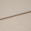 Beige woven fabric with regular small navy dash dots, folded once across center, lying flat on a neutral surface; close-up, even studio lighting highlighting its textured weave.