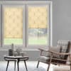 Beige roller blinds with curved pattern — left lowered, right partially lowered, filtering daylight into a gray living room with rattan armchair, cushion and round table with vases, grassy backyard view.