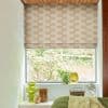 Beige wavy-patterned Roman blind lowered over the window, partly raised at the bottom; filtering daylight into a bedroom alcove with plants, glass vases on the sill and a green bedspread.