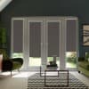French glass doors and sidelights with dark roller blinds covering most panes, revealing narrow garden view; glass-top coffee table sits on zigzag rug between green armchairs in a living room.