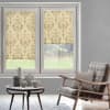 Patterned beige roller blinds with damask motif lowered over a double window; partially closed, filtering daylight; cozy living room with rattan armchair, coffee table with ceramics, grassy backyard visible.
