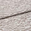 Decorative woven fabric with white and light beige abstract zebra-like pattern, tightly woven and folded across the center; lying as a layered textile sample in a close-up, evenly lit shot.