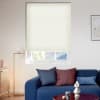 A cream honeycomb cellular blind, lowered over a recessed window and slightly raised, filtering soft daylight into a modern living room with blue sofa, cushions and a floor lamp.