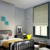 Green-and-white patterned Roman shade lowered over a black-framed window, filtering daylight; child’s grey-painted bedroom with black spindle bed, yellow chair, desk, plush toys and string lights.