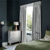 Pleated grey floor-length curtains on a black rod, pulled to each side and framing a tall sash window, admitting bright daylight; bedroom with dark teal walls, white dresser, green bedding.