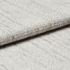 Light-gray textured fabric panel with subtle vertical stripes and stitched horizontal fold — folded over to form a crisp edge — close-up view with soft, even lighting on a neutral surface.