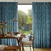 Teal textured full-length pleated curtains, parted slightly at center, framing a sliding glass door; filtering soft daylight into a dining nook with wooden table, chairs, pendant lamp and garden view.