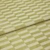 Folded green-and-cream checkered rug, raised pile squares forming a staggered grid; folded edge overlapping, displaying tufted texture and subtle wear in a close-up, evenly lit studio view.
