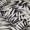 A folded decorative fabric with cream palm-leaf print on a black background; the layers overlap, emphasizing texture and weave, shown in a close-up under soft, even lighting.