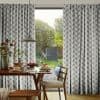 Pleated floor-to-ceiling curtains with gray stepped pattern, parted centrally to reveal a sunlit garden. They frame a breakfast table with pancakes, pendant lamp and wooden chairs in a dining area.