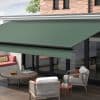 Green fabric retractable awning mounted above glass doors, extended with black roller and front bar, shading a wooden patio with lounge seating, round table, and brick-backed house in daylight.