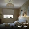 A white Roman blind lowered across a small rectangular window, diffusing soft daylight; in a neutral-toned bedroom with a woven pendant lamp, wooden headboard, cushions and a fairy-lit shelf with framed art and ornaments.
AS SEEN IN Ideal Home