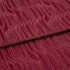 Burgundy fabric with raised, irregular pale-pink wavy lines (textured pile), folded once across the center, lying flat in a close-up, evenly lit studio view, showing pattern and subtle shadows.