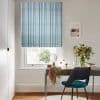 Blue-and-white striped Roman blind, lowered with neat folds, filtering soft daylight into a small home office featuring a wooden desk, teal chair and a vase of flowers.