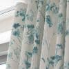 Pleated fabric drapes with a teal watercolor tree pattern, hanging closed over a window; filtering soft daylight into an interior space beneath a white cornice.