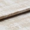 Beige-and-white distressed-pattern fabric panel with a horizontal fold, resembling a Roman blind; photographed close-up on a neutral surface under soft, even lighting.
