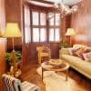 Wooden plantation shutters on a bay window, closed with angled louvers filtering soft daylight; set in a wood‑paneled living room with warm lamps, beige sofa, round coffee table, and sheepskin rug.