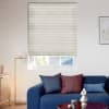 Cream pleated cellular blind lowered over window, filtering daylight and slightly raised to reveal lower panes; in a bright living room with a blue sofa, cushions, floor lamp, coffee table.